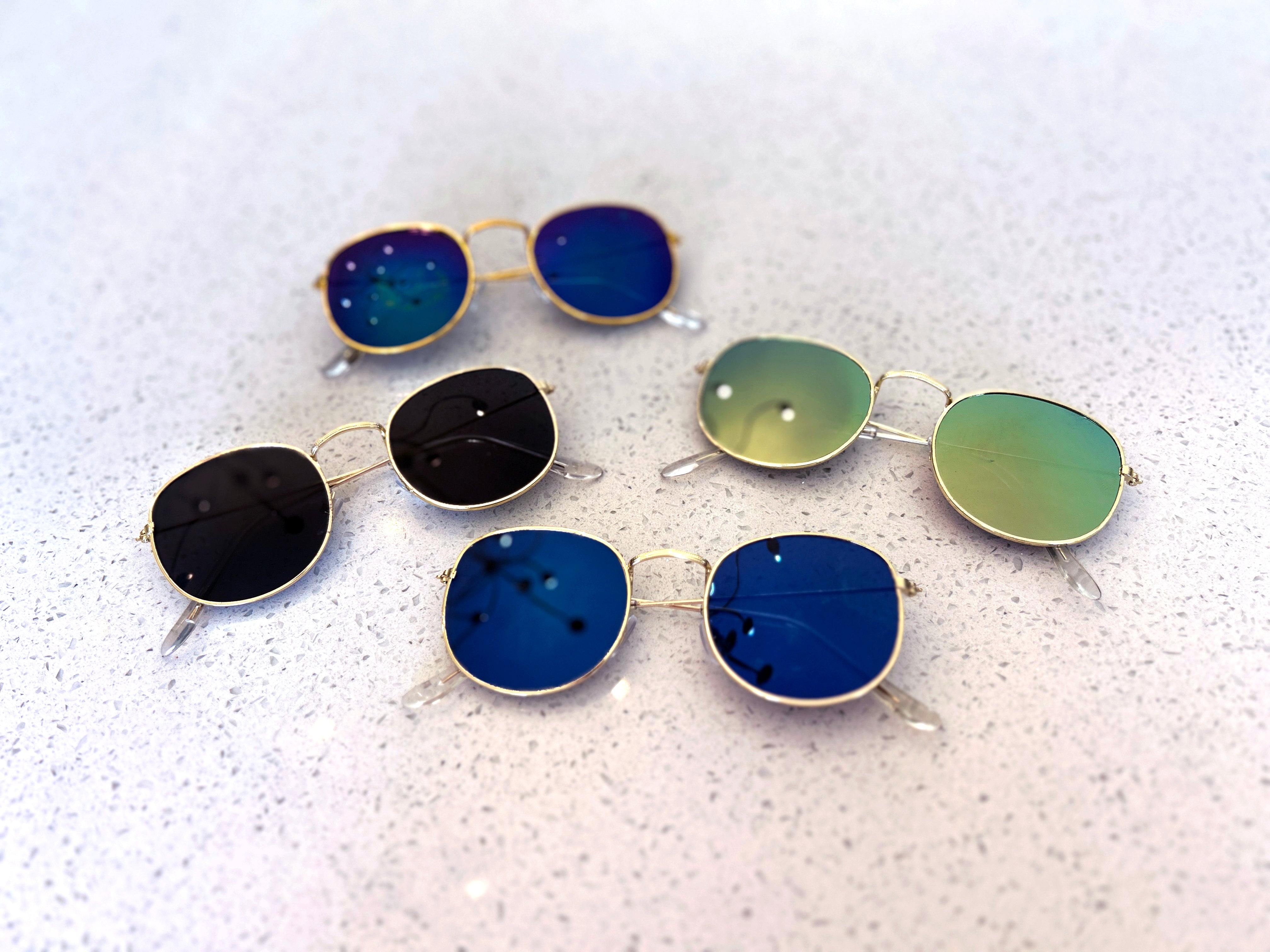 Set of round sunglasses with blue, green, and black lenses on a textured white surface
